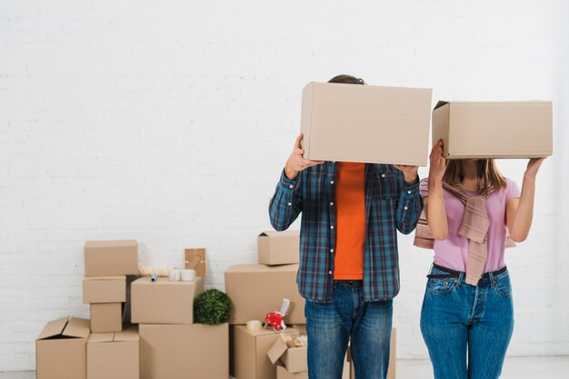 Junge Paare, die ihre Gesichter mit Pappschachteln im neuen Haus verstecken