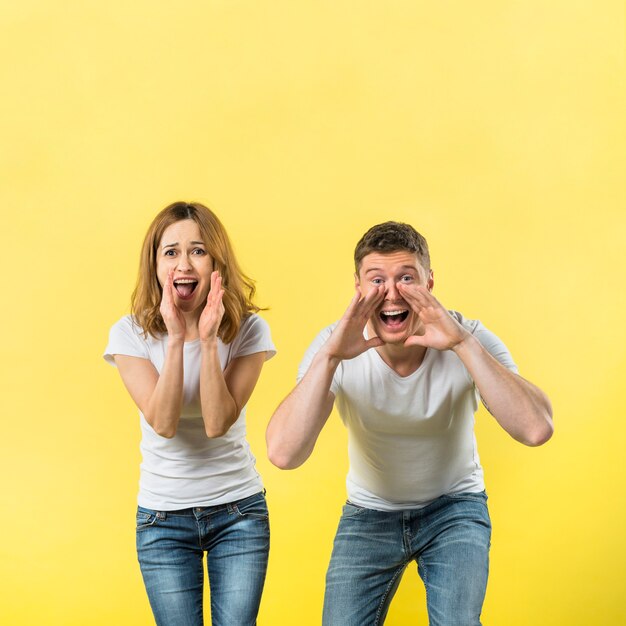 Junge Paare, die laut gegen gelben Hintergrund schreien