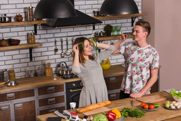 Junge Paare, die mit dem Grün in der Küche täuschen