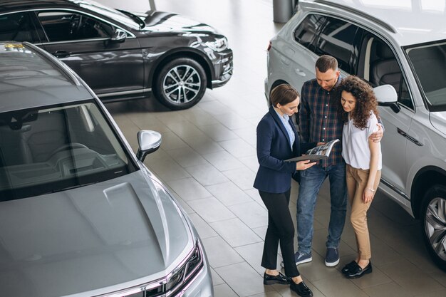 Junge Paare, die mit einem Verkäufer in einem Autosalon sprechen