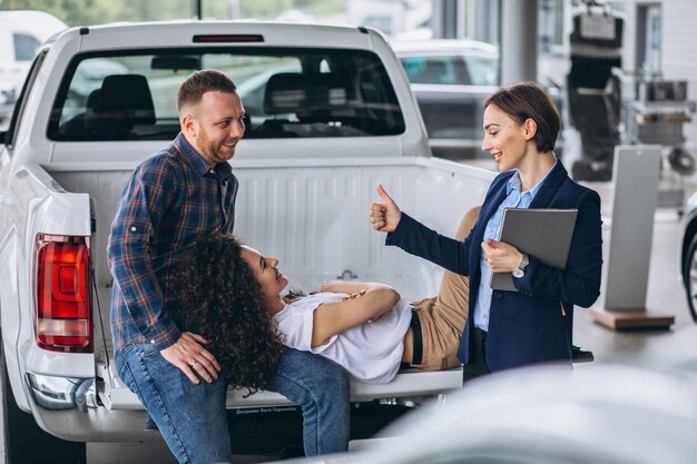 Junge Paare, die mit einem Verkäufer in einem Autosalon sprechen