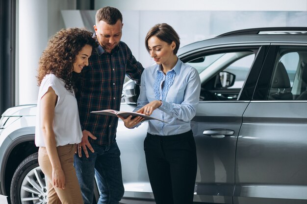 Junge Paare, die mit einem Verkäufer in einem Autosalon sprechen