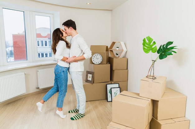 Junge Paare, die mit Pappschachteln in ihrem neuen Haus sich küssen