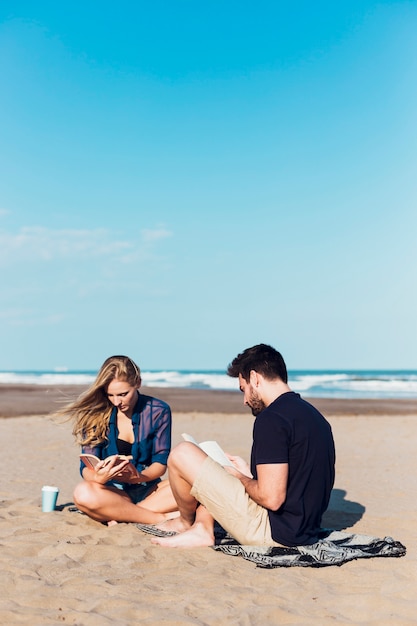Junge Paare, die nahe Meer lesen