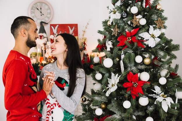 Junge Paare, die nahe Weihnachtsbaum umfassen