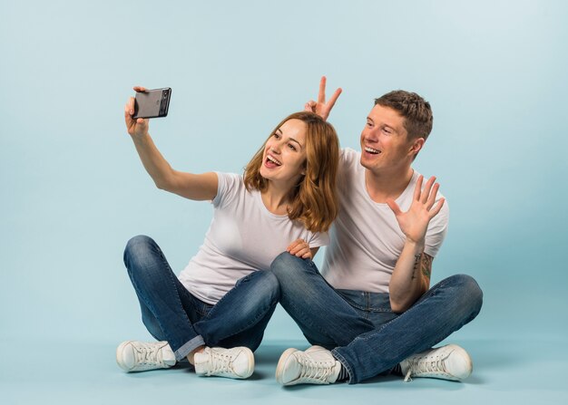 Junge Paare, die selfie am Handy gegen blauen Hintergrund nehmen