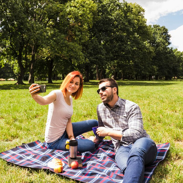 Junge Paare, die selfie am Handy Picknick am im Freien nehmen