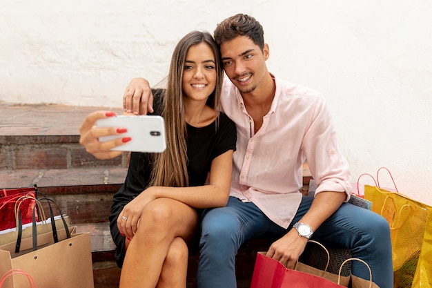 Junge Paare, die selfies nahe bei Einkaufstaschen nehmen