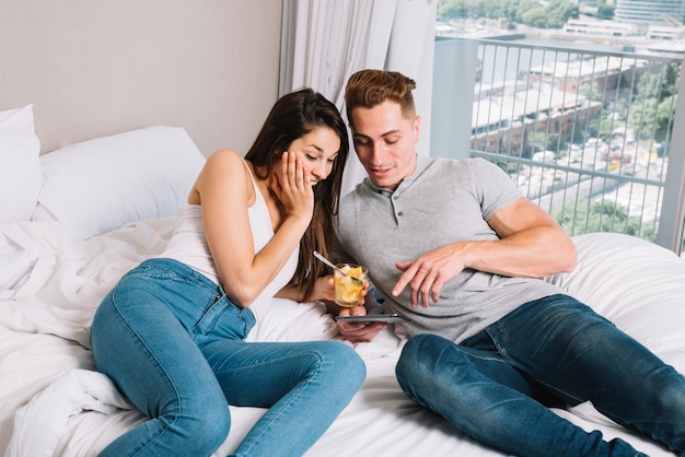 Junge Paare, die Smartphone auf Bett betrachten