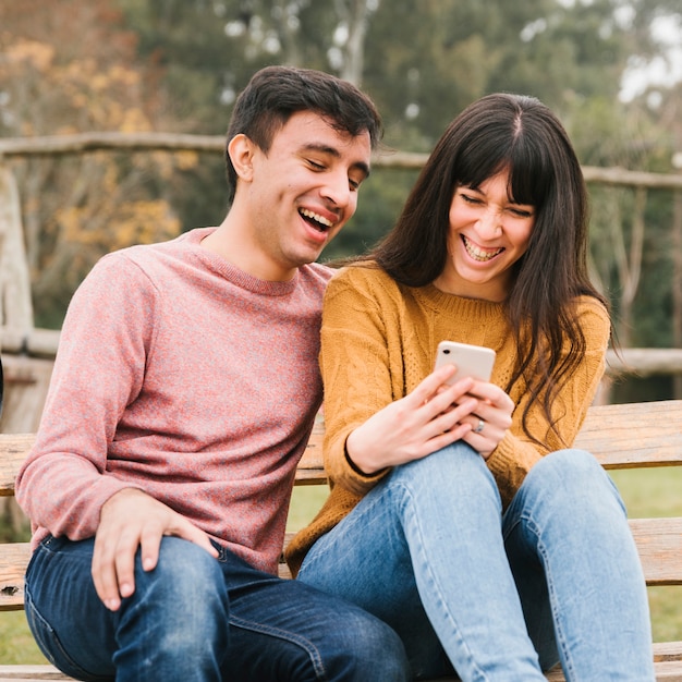 Junge Paare, die Smartphoneschirm betrachtend lachen