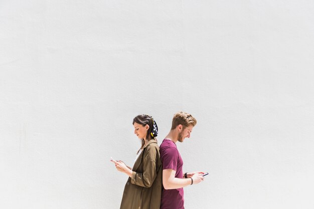 Junge Paare, die zurück zu Rückseite unter Verwendung des Mobiltelefons stehen