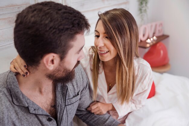 Junge Paare in den Pyjamas, die auf Bett sitzen