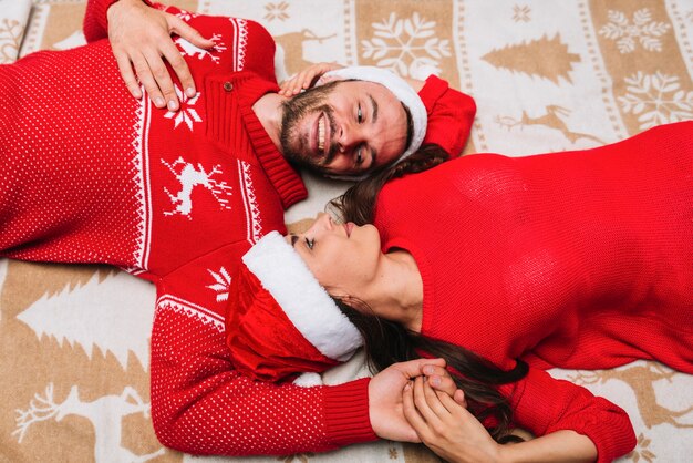 Junge Paare in den Weihnachtshüten, die auf Plaid liegen