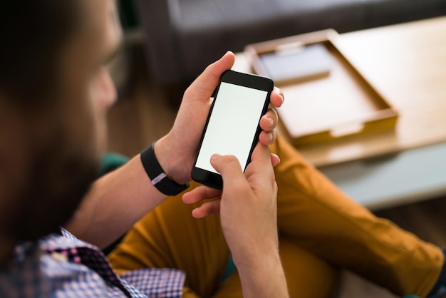 Junge Person, die ihr Smartphone benutzt, während sie zu Hause sitzt und auf einen leeren Bildschirm mit Copyspace blickt