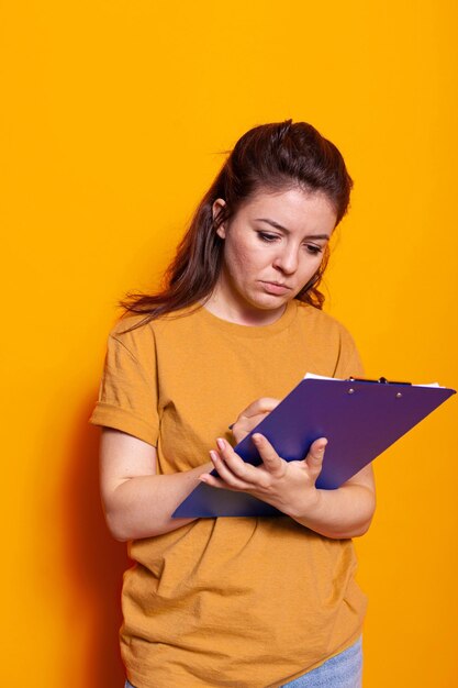 Junge Person, die Notizen zu Notizbuchdateien mit Stift im Studio macht. Konzentrierte Frau, die auf Lehrbuchpapieren schreibt, Dokumente und Papierkram über das Projekt in der Notizblock-Zwischenablage unterschreibt.