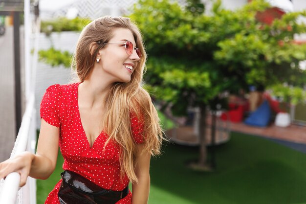 Junge romantische Frau, die Landschaft des tropischen Erholungsortes genießt, im Park steht und lächelt