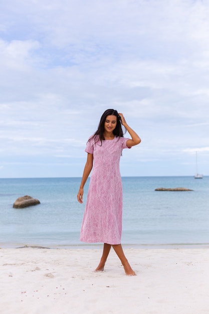 Junge romantische Frau mit langen dunklen Haaren in einem Kleid am Strand lächelnd und lachend, eine schöne Zeit allein habend