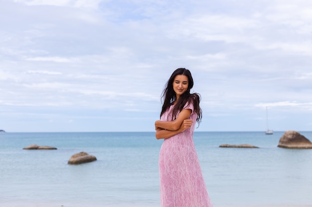 Junge romantische Frau mit langen dunklen Haaren in einem Kleid am Strand lächelnd und lachend, eine schöne Zeit allein habend