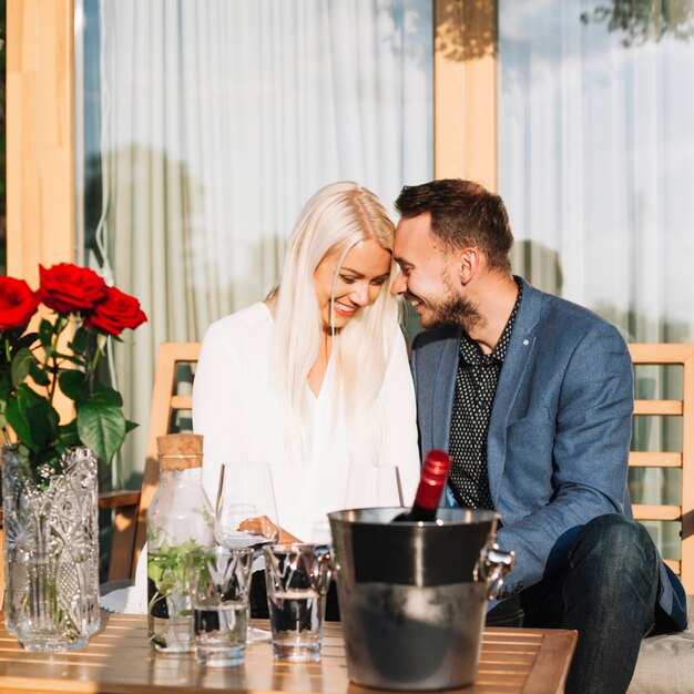 Junge romantische Paare, die hinter der Tabelle mit Weinflasche im Eiseimer sitzen