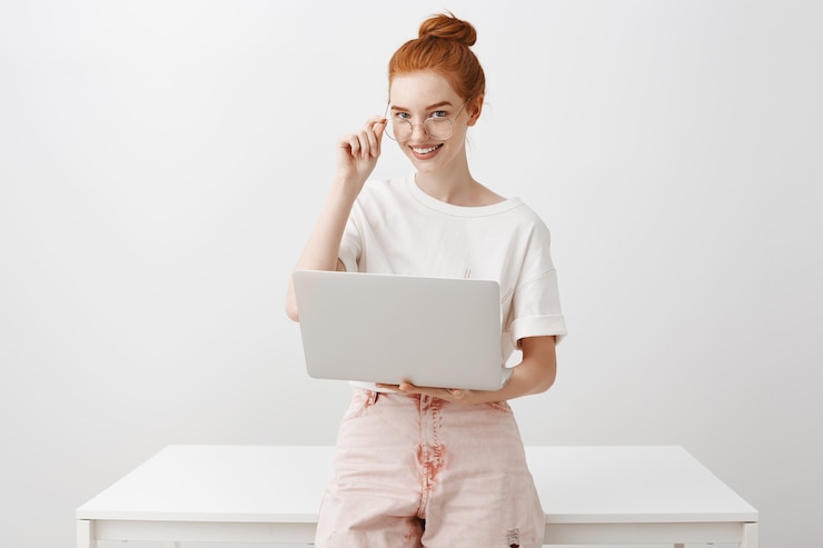 Kostenlose Foto junge rothaarige frau, die mit laptop arbeitet und brille trägt