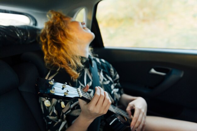 Junge Rothaarigefrau, die Ukulele in der Maschine spielt