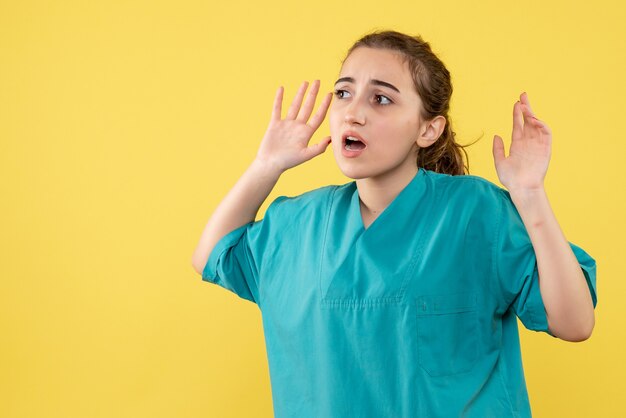 Junge Ärztin der Vorderansicht im medizinischen Anzug auf gelbem Hintergrund