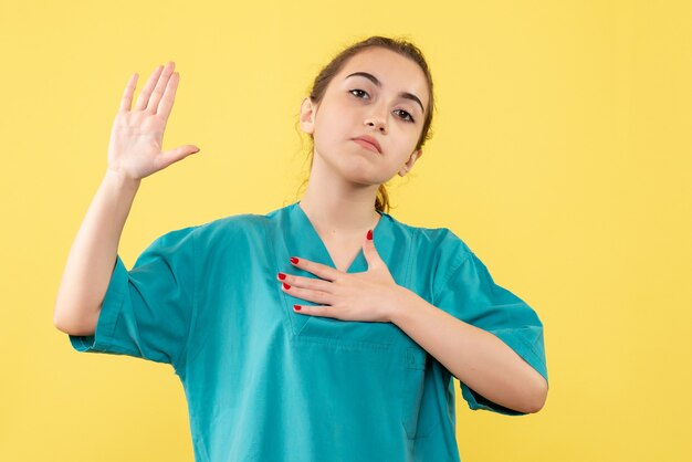 Junge Ärztin der Vorderansicht im medizinischen Anzug auf gelbem Hintergrund