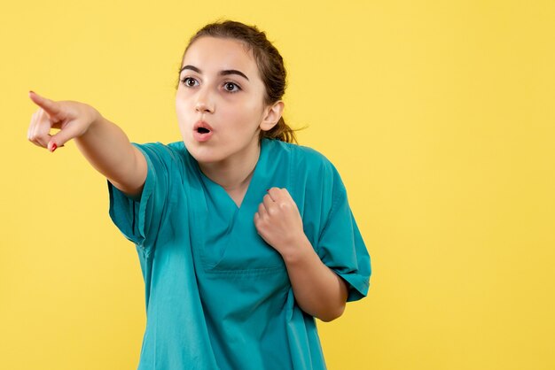 Junge Ärztin der Vorderansicht im medizinischen Anzug, der auf gelben Hintergrund zeigt