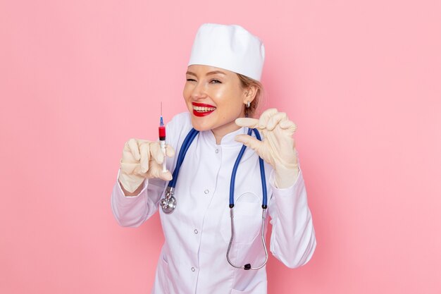 Junge Ärztin der Vorderansicht im weißen medizinischen Anzug mit blauem Stethoskop, das Injektion auf den weiblichen Job des medizinischen Krankenhausarbeiters der rosa Raummedizin hält