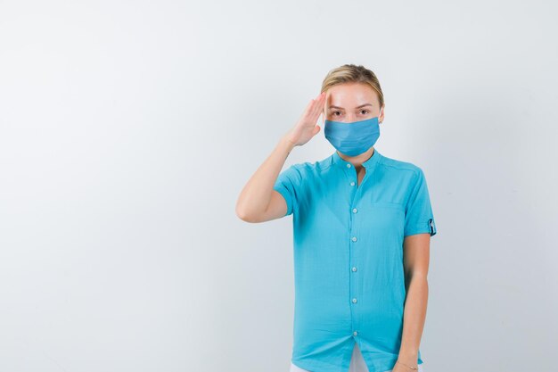 Junge Ärztin, die Hand auf dem Kopf in medizinischer Uniform, Maske hält und selbstbewusst aussieht