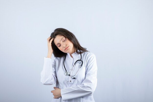 Junge Ärztin mit Stethoskop mit Kopfschmerzen auf weißer Wand.