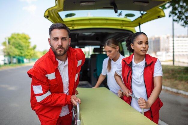 Junge Sanitäter, die in Eile eine Krankentrage aus dem Auto bewegen Sanitäter in Uniform, die eine Trage aus dem Krankenwagen nehmen