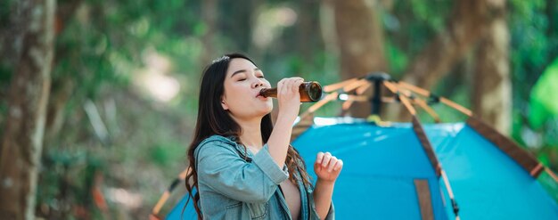 Junge schöne asiatische Frauen und befreundete Reisende entspannen sich vor dem Campingzelt. Sie unterhalten sich gerne und trinken Bier mit Spaß und Freude zusammen