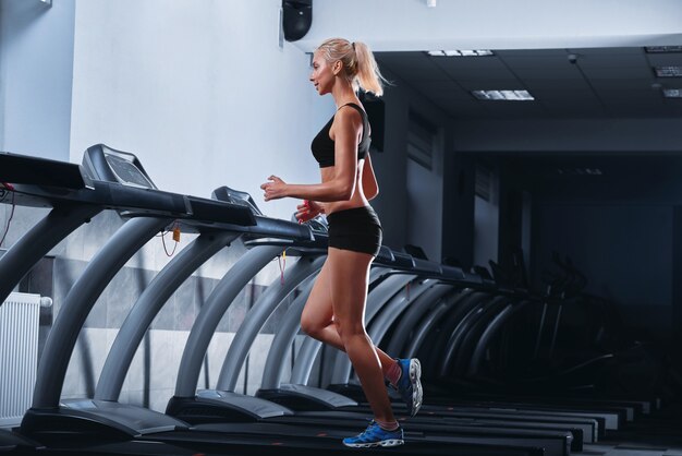 Junge schöne athletische Frau, die auf einem Laufband an der Turnhalle läuft