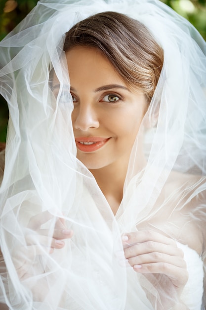 Junge schöne blonde Braut im Hochzeitskleid und im Schleier lächelnd.