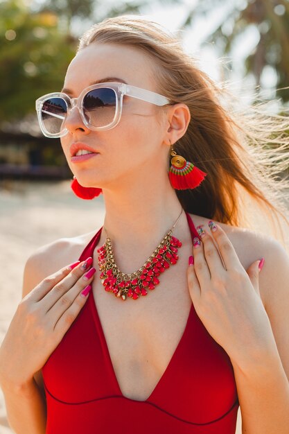 Junge schöne blonde Frau, die am Strand im roten Badeanzug, Sonnenbrille sonnenbad