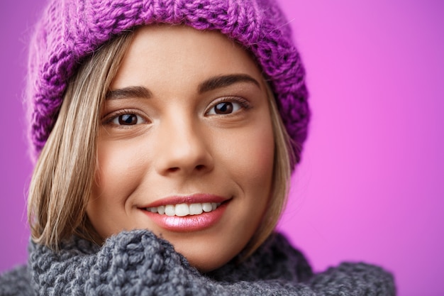 Junge schöne blonde Frau in Strickmütze und Pullover lächelnd auf Veilchen.