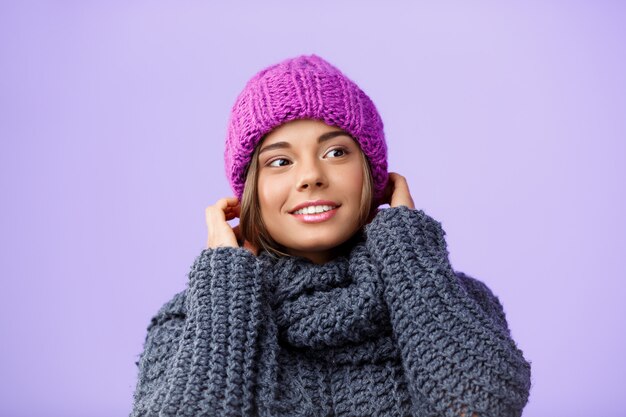 Junge schöne blondhaarige Frau in der Strickmütze und im Pullover lächelnd, die Seite auf Veilchen schauend.