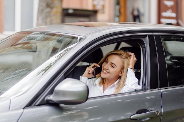 Junge schöne Blondine im Auto mit Telefon