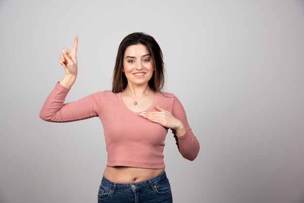 Junge schöne brünette Frau stehend und Finger nach oben zeigend.