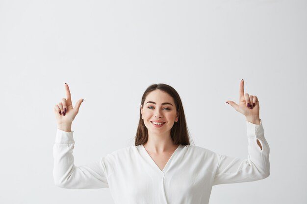 Junge schöne brünette Geschäftsfrau lächelnd zeigende Finger nach oben.