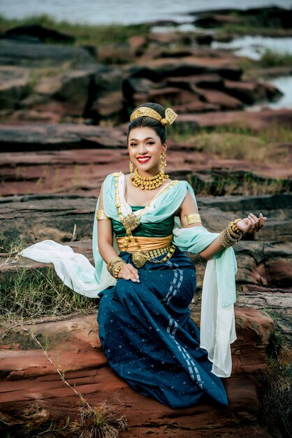 Junge schöne Frau des Porträts, die in der traditionellen Tracht mit dem Ornament trägt, das in der Natur in Thailand aufwirft?