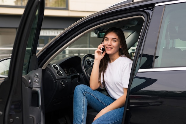 Junge schöne Frau, die am Telefon spricht, das im Auto sitzt