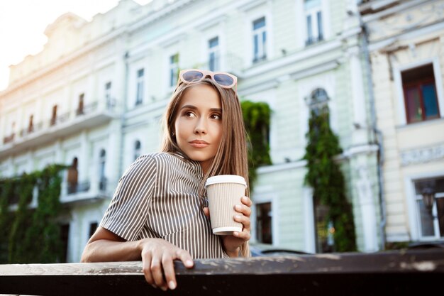 Junge schöne Frau, die auf Bank sitzt und Kaffee hält