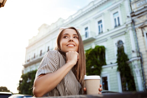 Junge schöne Frau, die auf Bank sitzt und Kaffee hält