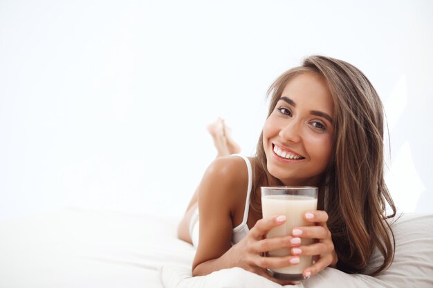 Junge schöne Frau, die auf Bett liegt, Kaffee trinkend, lächelnd