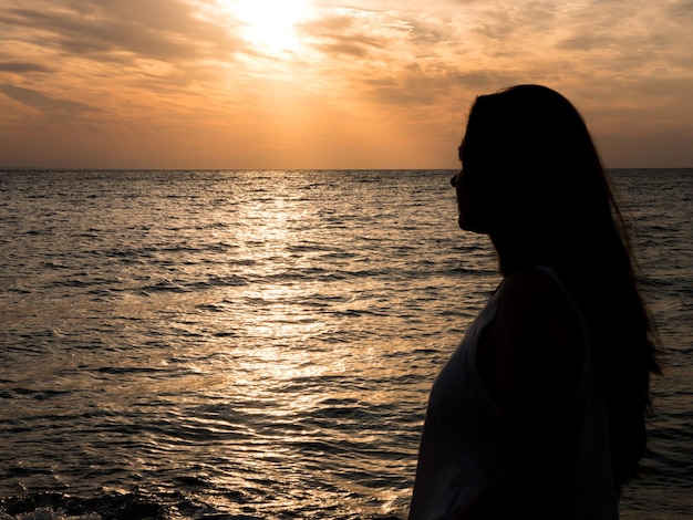 Junge schöne Frau, die den Sonnenuntergang am Meer bewundert. Schöne Frau mit der Natur vereint