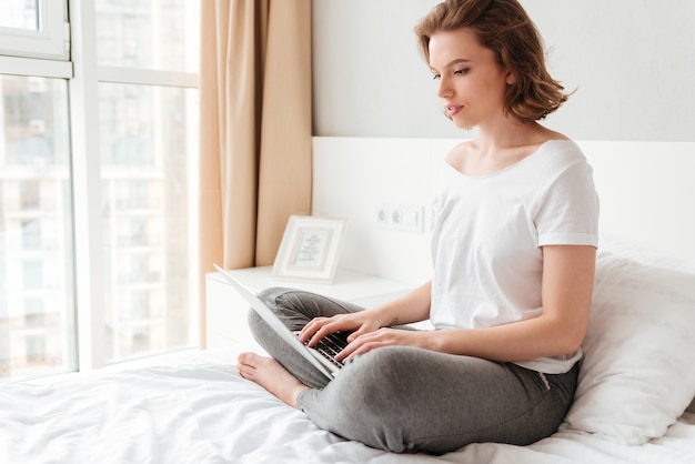 Junge schöne Frau, die drinnen mit Laptop sitzt