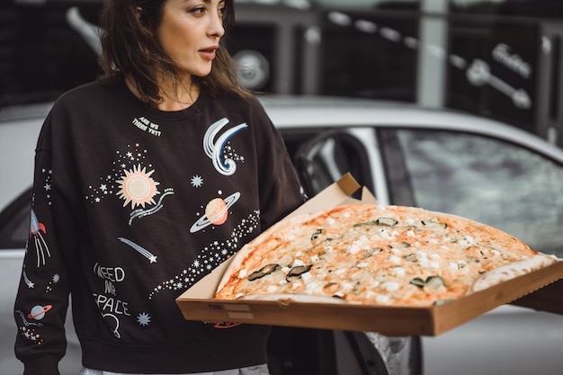 Junge schöne Frau, die eine Scheibe der Pizza auf Stadtstraße isst