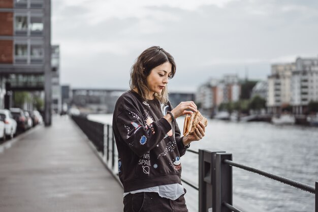 Junge schöne Frau, die eine Scheibe der Pizza auf Stadtstraße isst